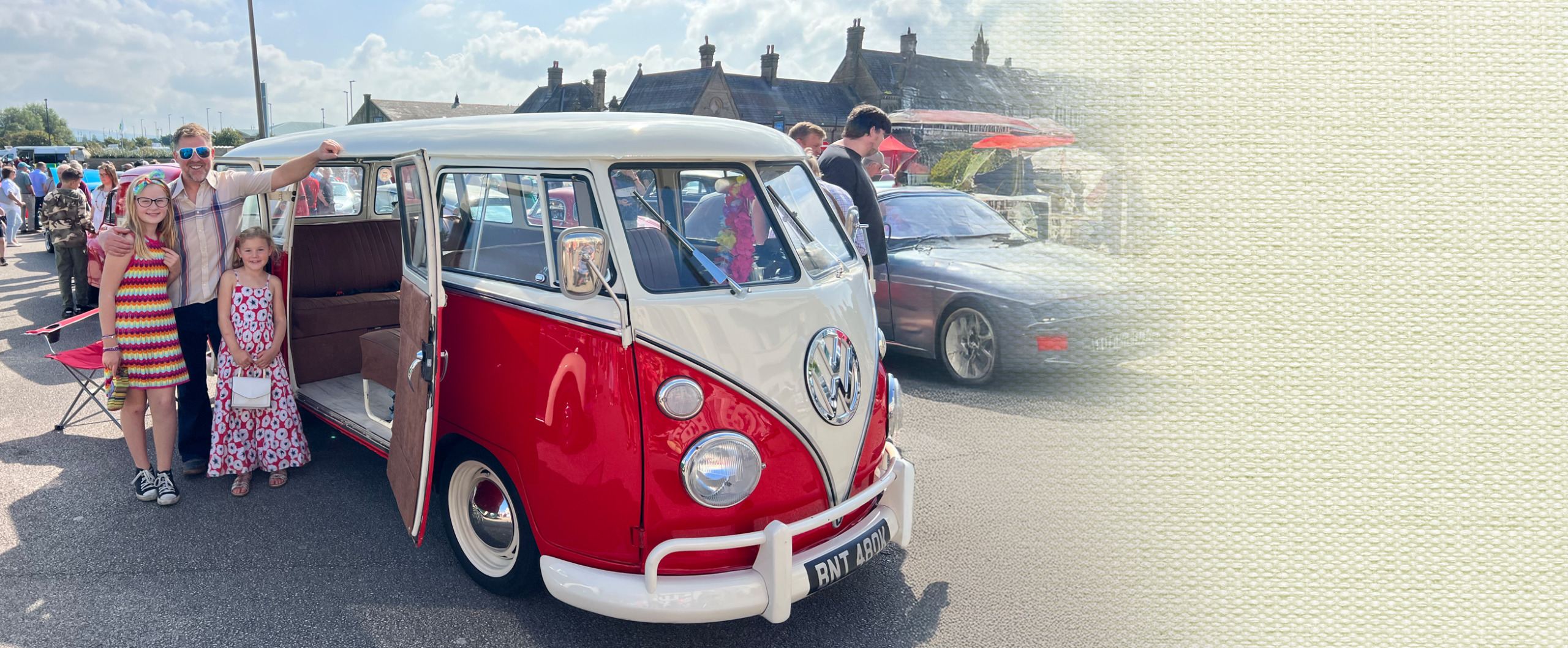 Red and white 1972 split-screen VW campervan parked at a classic car show